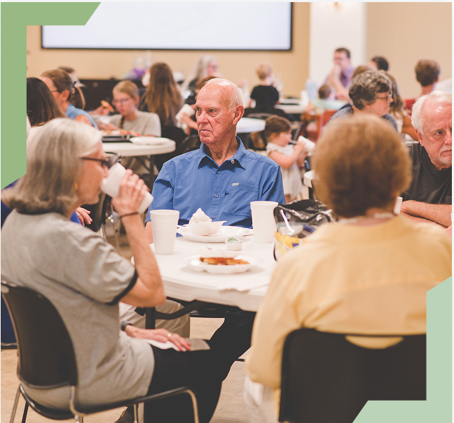 Members of the congregation sharing a meal together around tables in the fellowship hall
